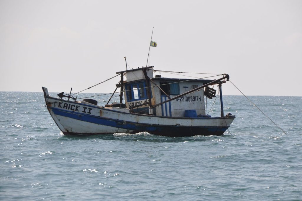 A rustic fishing boat flying the Brazilian flag is captured sailing on the open sea with a clear horizon.
