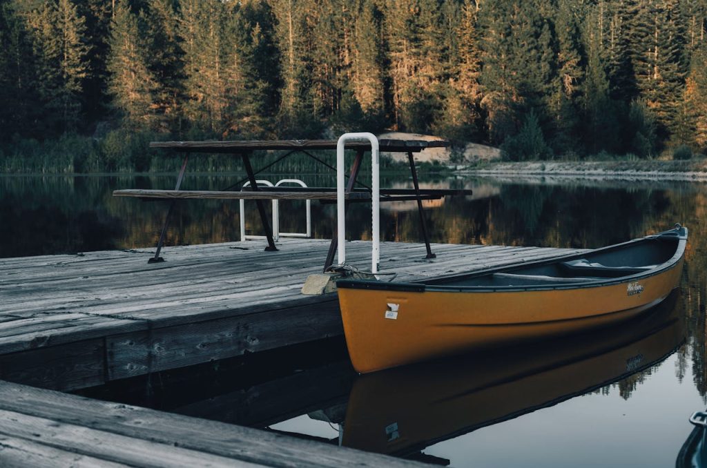 pexels photo 13545074 A peaceful scene of a canoe docked on a wooden pier by a calm forested lake.